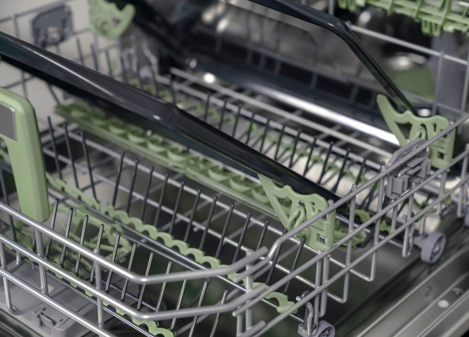 The bottom rack of a dishwasher featuring two green side hooks designed to organize and secure trays.
